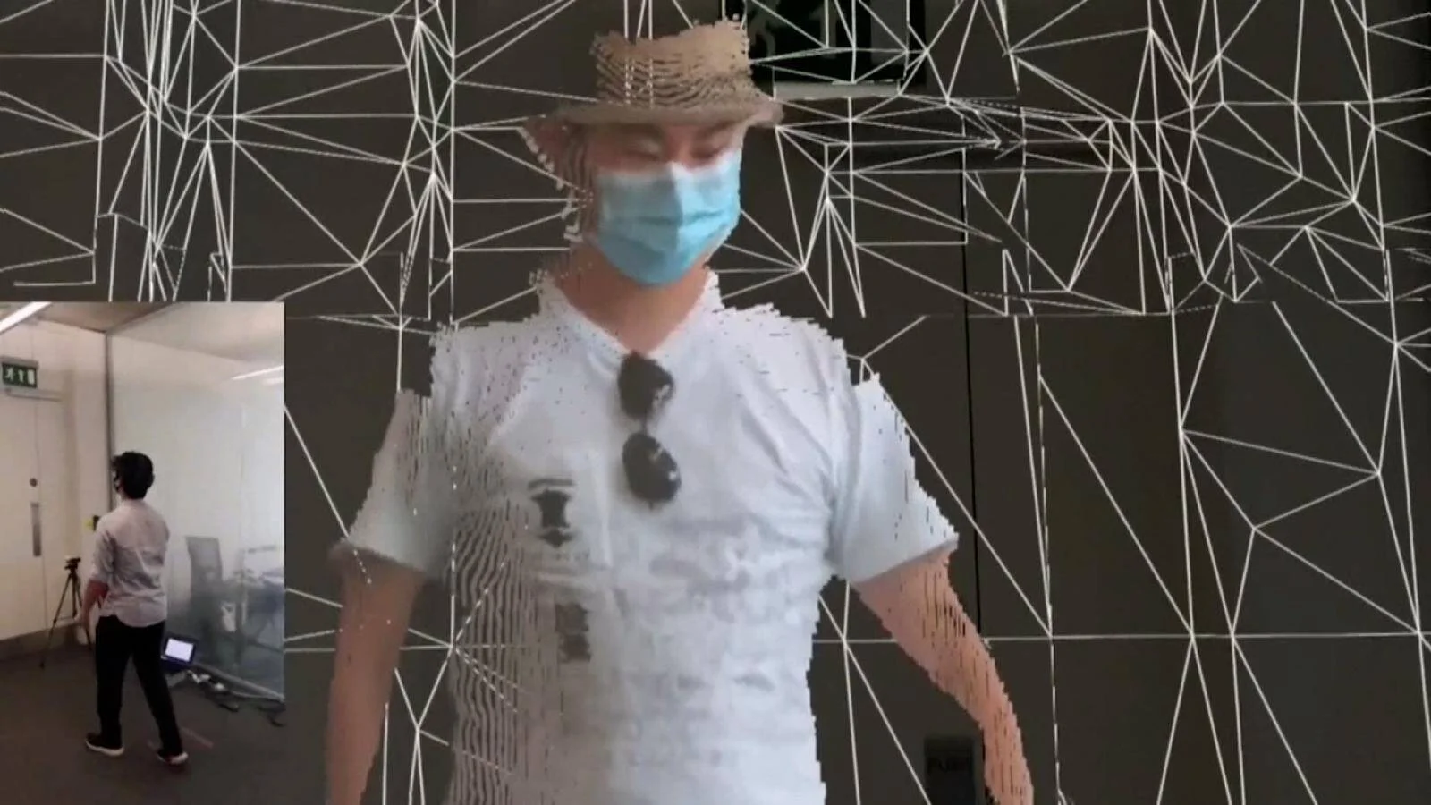 Persona con mascarilla, sombrero y camiseta blanca frente a una pantalla con gráficos de red geométrica, en un entorno de arte interactivo.