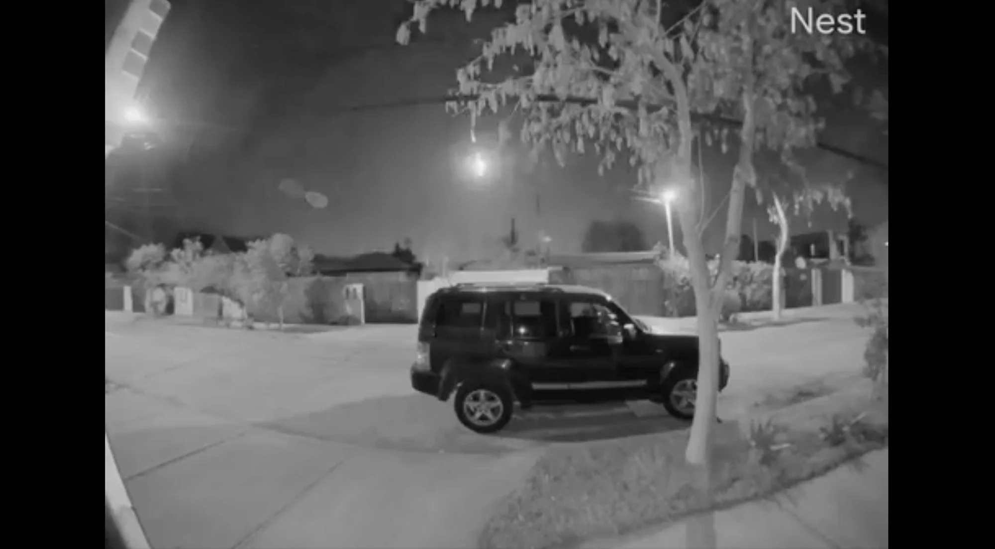 Captura de cámara de seguridad Nest que muestra un SUV oscuro estacionado en una calle residencial durante la noche.