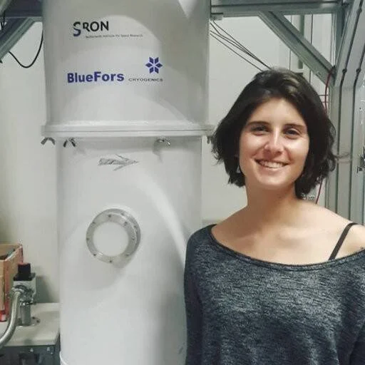 Mujer sonriente posando junto a un sistema criogénico BlueFors en instalación del Instituto SRON de Investigación Espacial.