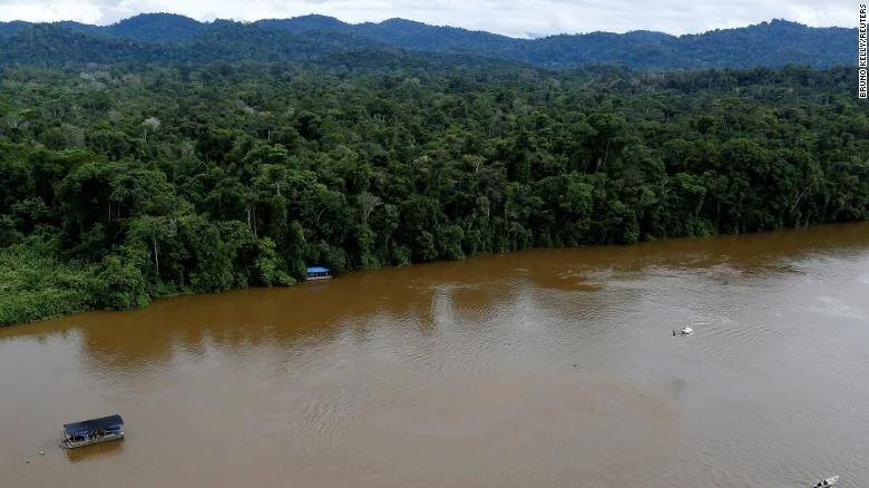 Vista aérea de un río de aguas turbias en la Amazonía con dos embarcaciones y densa selva tropical en la orilla.