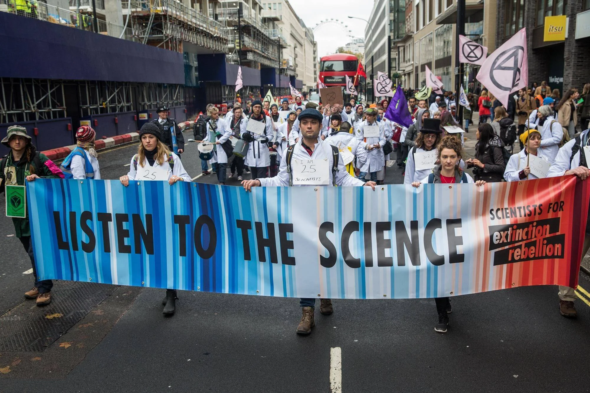 Científicos con batas blancas marchan por una calle de Londres sosteniendo una pancarta que dice 'Listen to the Science' de Extinction Rebellion.
