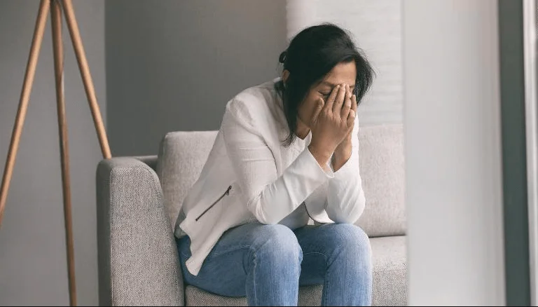 Mujer sentada en un sofá cubre su rostro con las manos en señal de angustia o llanto.