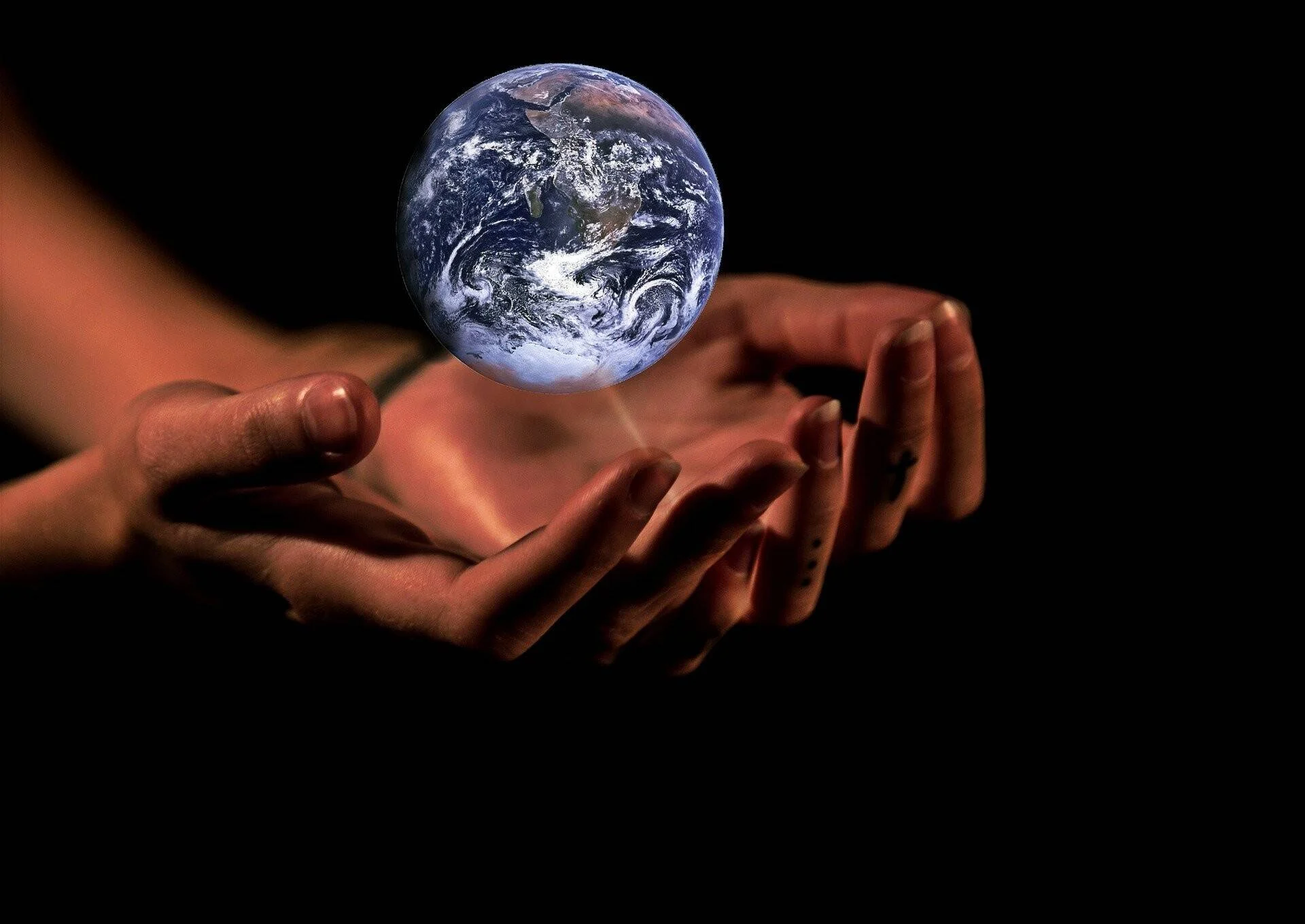 Dos manos abiertas sostienen una miniatura del planeta Tierra flotando sobre ellas, sobre fondo negro.