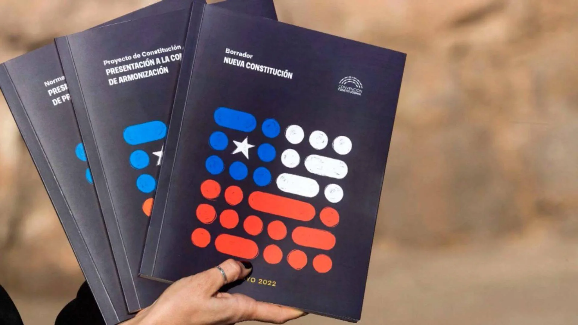 Una mano sostiene varios ejemplares del borrador de la Nueva Constitución de Chile de mayo de 2022, publicado por la Convención Constitucional.