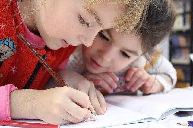 Dos niñas en edad escolar escriben juntas en un cuaderno, concentradas en la tarea.