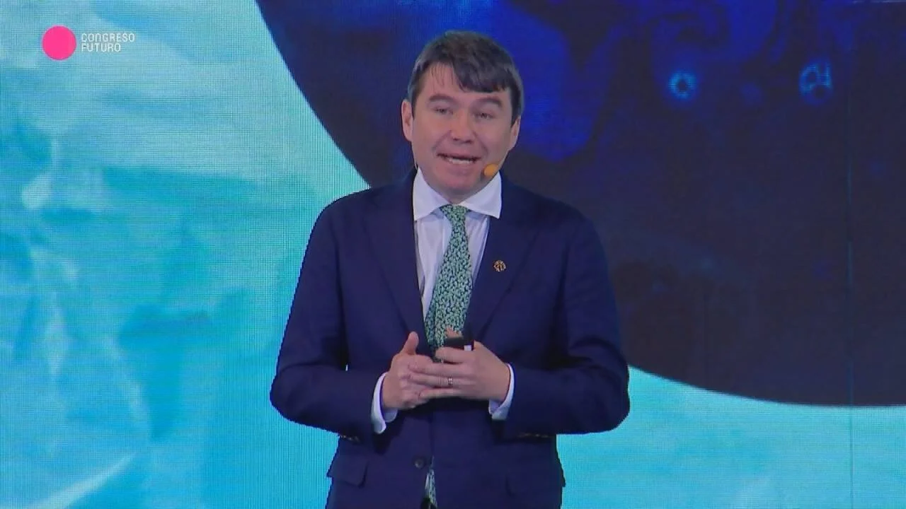 Hombre con traje azul y corbata verde habla en el escenario del Congreso Futuro ante un fondo iluminado en azul.