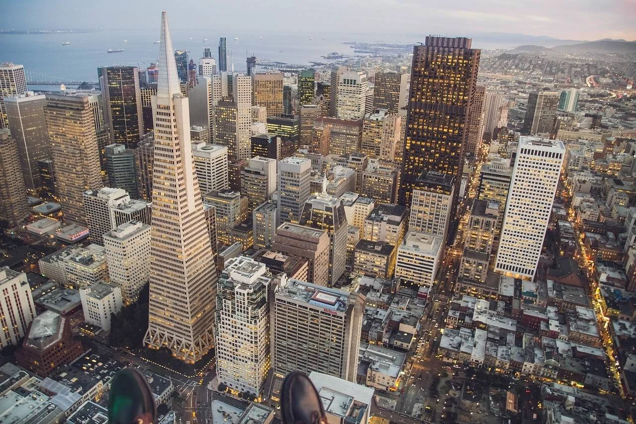 Panorámica aérea del centro de San Francisco al atardecer, con la Pirámide Transamerica destacando entre los rascacielos iluminados y la bahía al fondo.