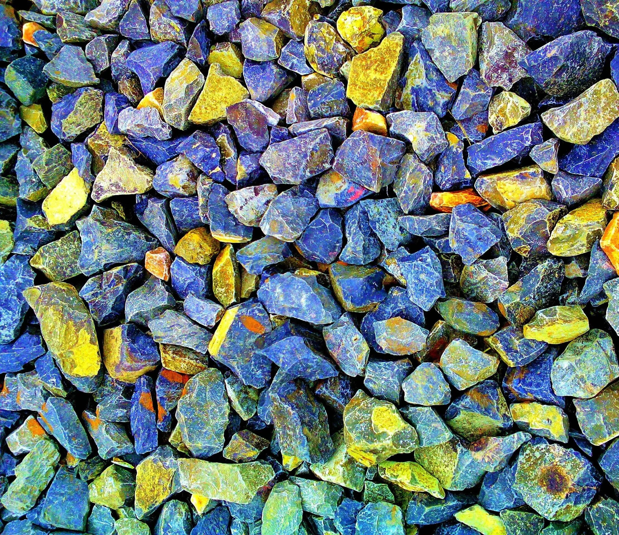 Acumulación de rocas irregulares en tonos azules, amarillos y verdes con colores vivos y saturados.