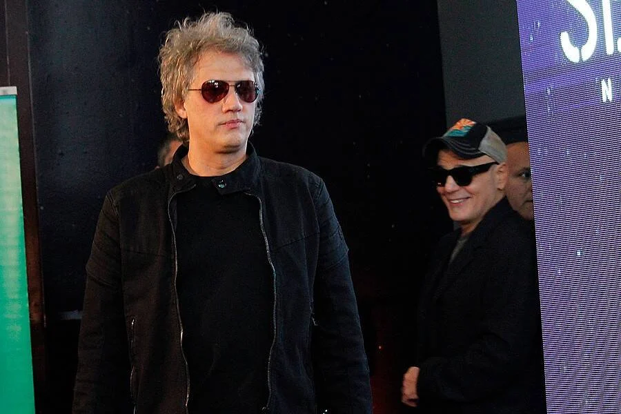 Dos hombres con lentes de sol y ropa negra caminan en lo que parece ser un evento o backstage.