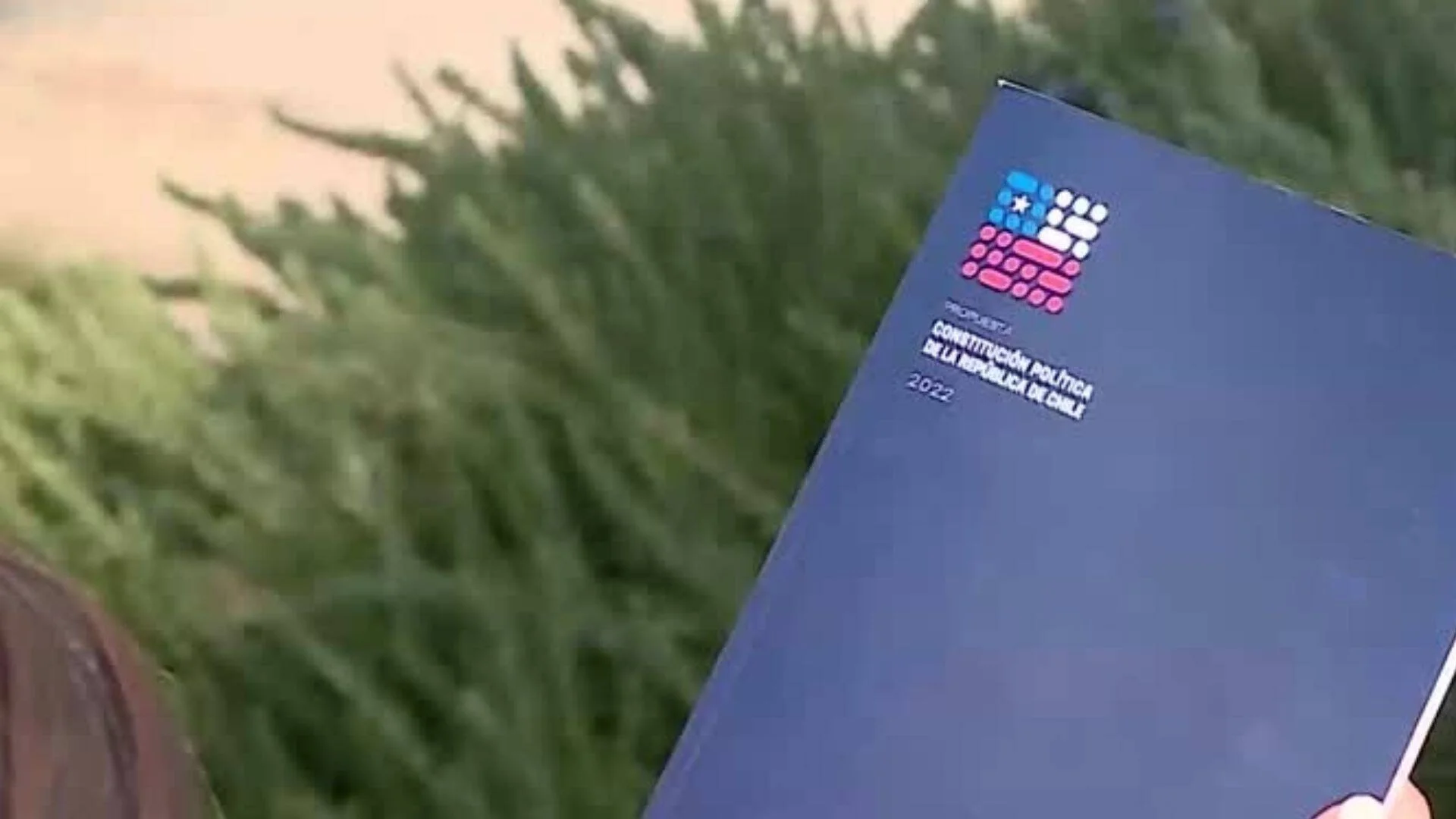 Mano sosteniendo el documento de propuesta de Constitución Política de la República de Chile 2022, con portada azul.