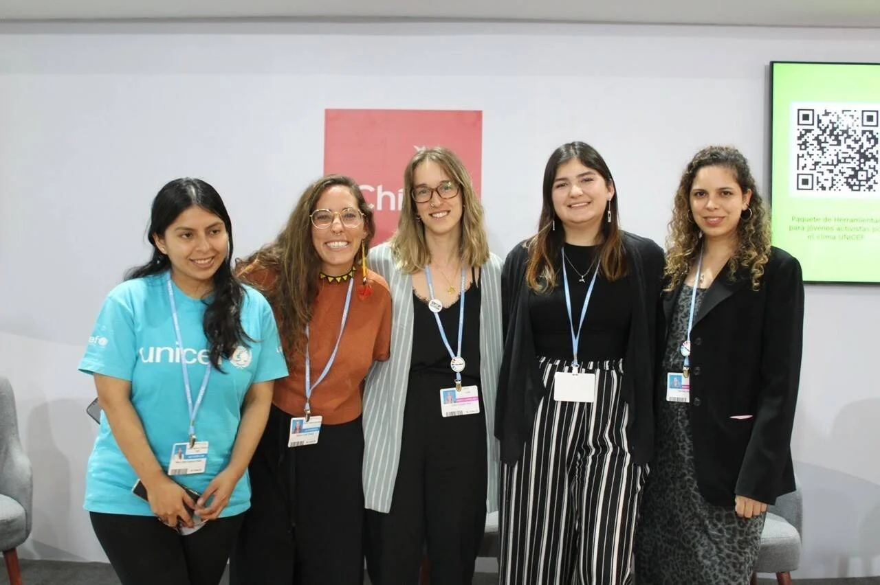 Cinco jóvenes con credenciales posan frente al stand de UNICEF Chile junto a una pantalla con código QR sobre activismo climático.