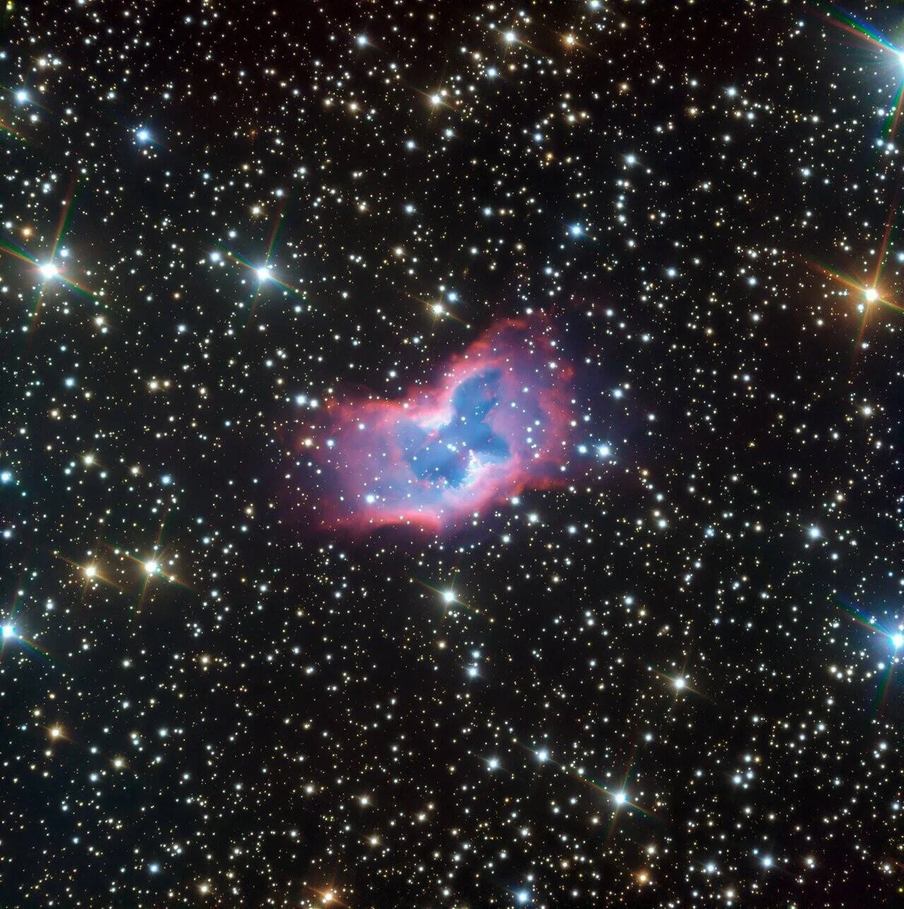 Nebulosa planetaria con nubes de gas en tonos azul y rojo rodeada de miles de estrellas en el fondo del espacio.