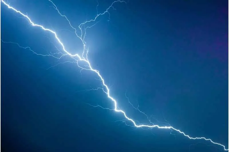 Rayo eléctrico brillante ramificado cruzando un cielo nocturno de tonos azul intenso.