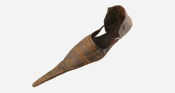 Zapato antiguo de cuero marrón con punta extremadamente larga y estrecha, de estilo medieval, con decoración grabada.