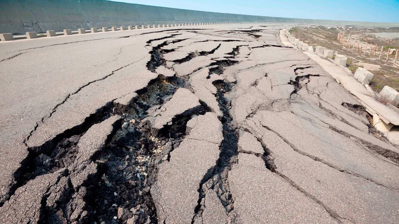 Carretera de asfalto severamente agrietada y hundida tras un sismo, con grandes fisuras que atraviesan toda la calzada.