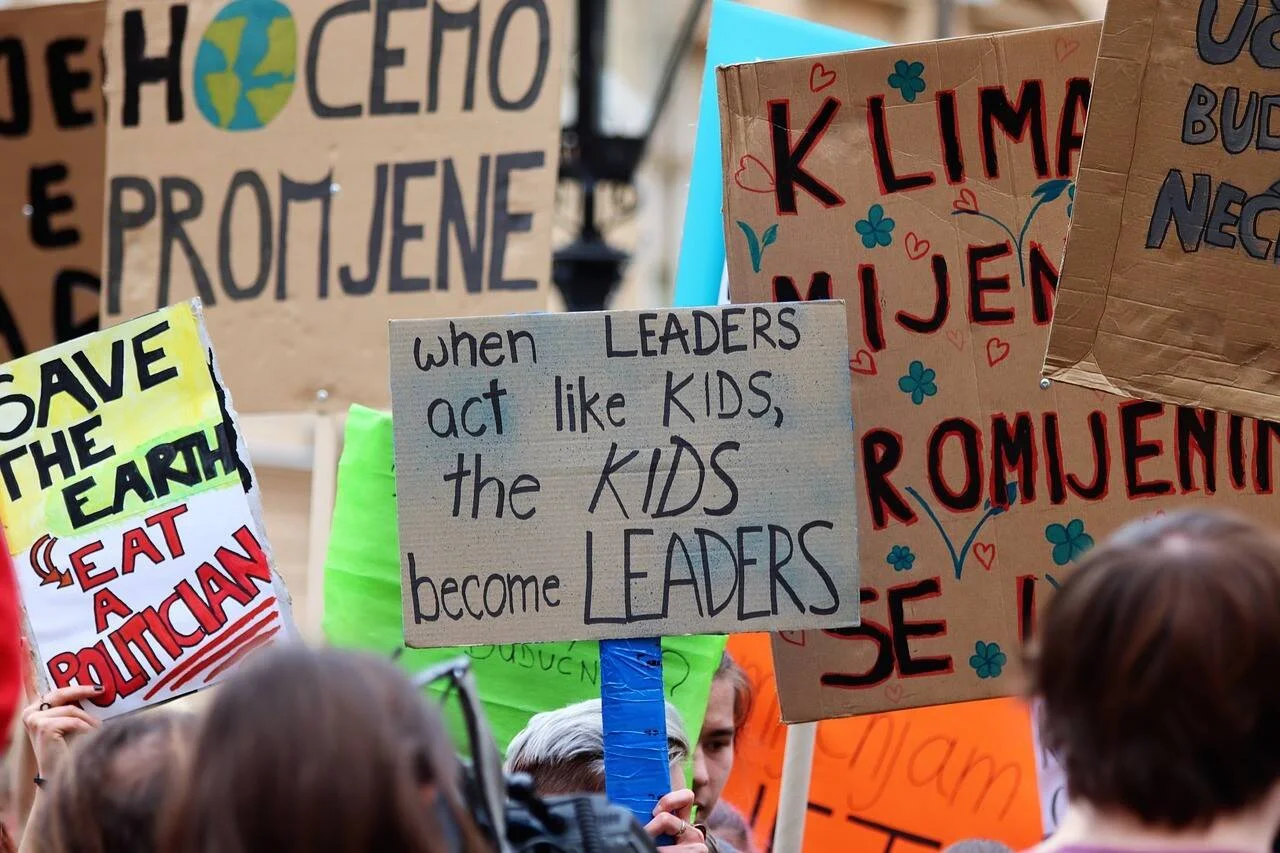 Manifestantes sostienen carteles sobre cambio climático con mensajes como 'when leaders act like kids, the kids become leaders' y 'Save the Earth'.
