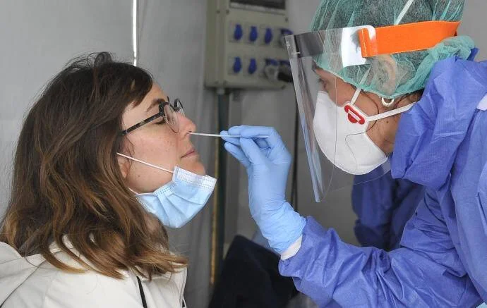 Profesional sanitaria con equipo de protección realiza un hisopado nasal a una mujer con mascarilla para detectar COVID-19.