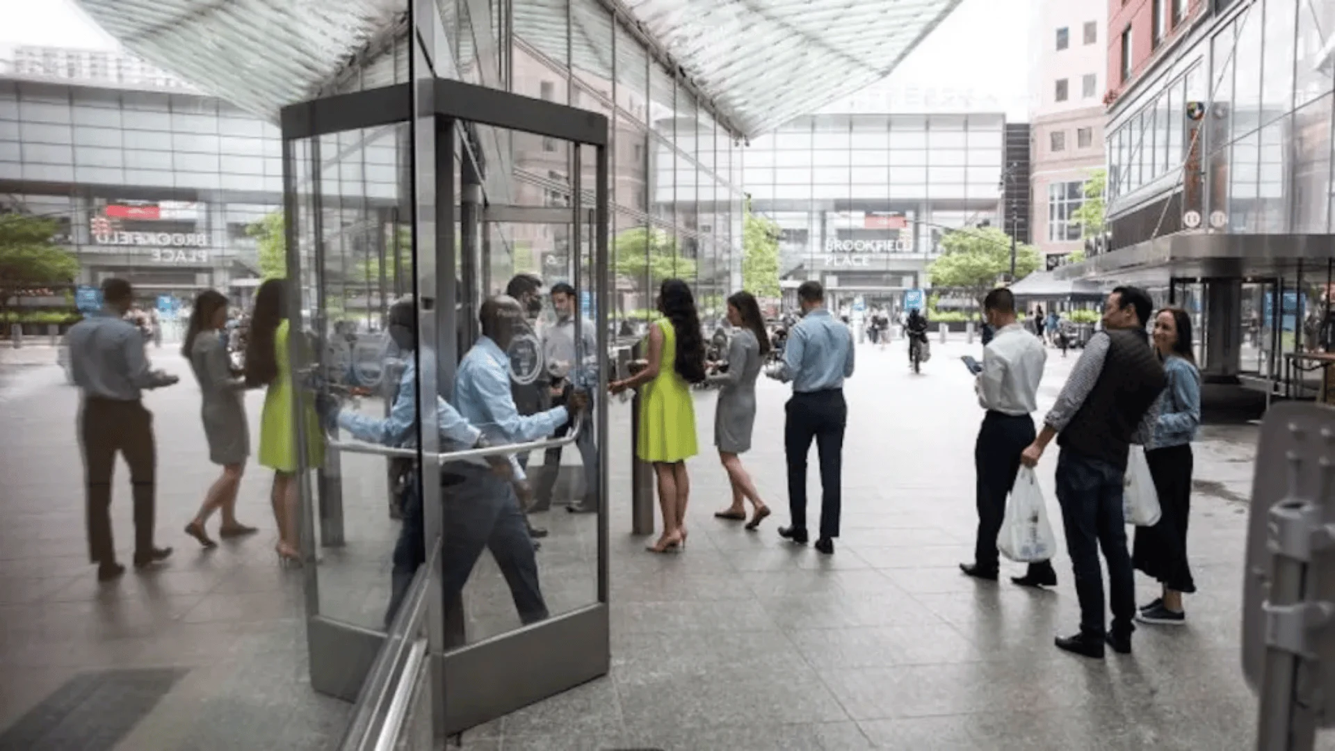 Trabajadores y visitantes hacen fila frente a una puerta giratoria de vidrio en la plaza de Brookfield Place.