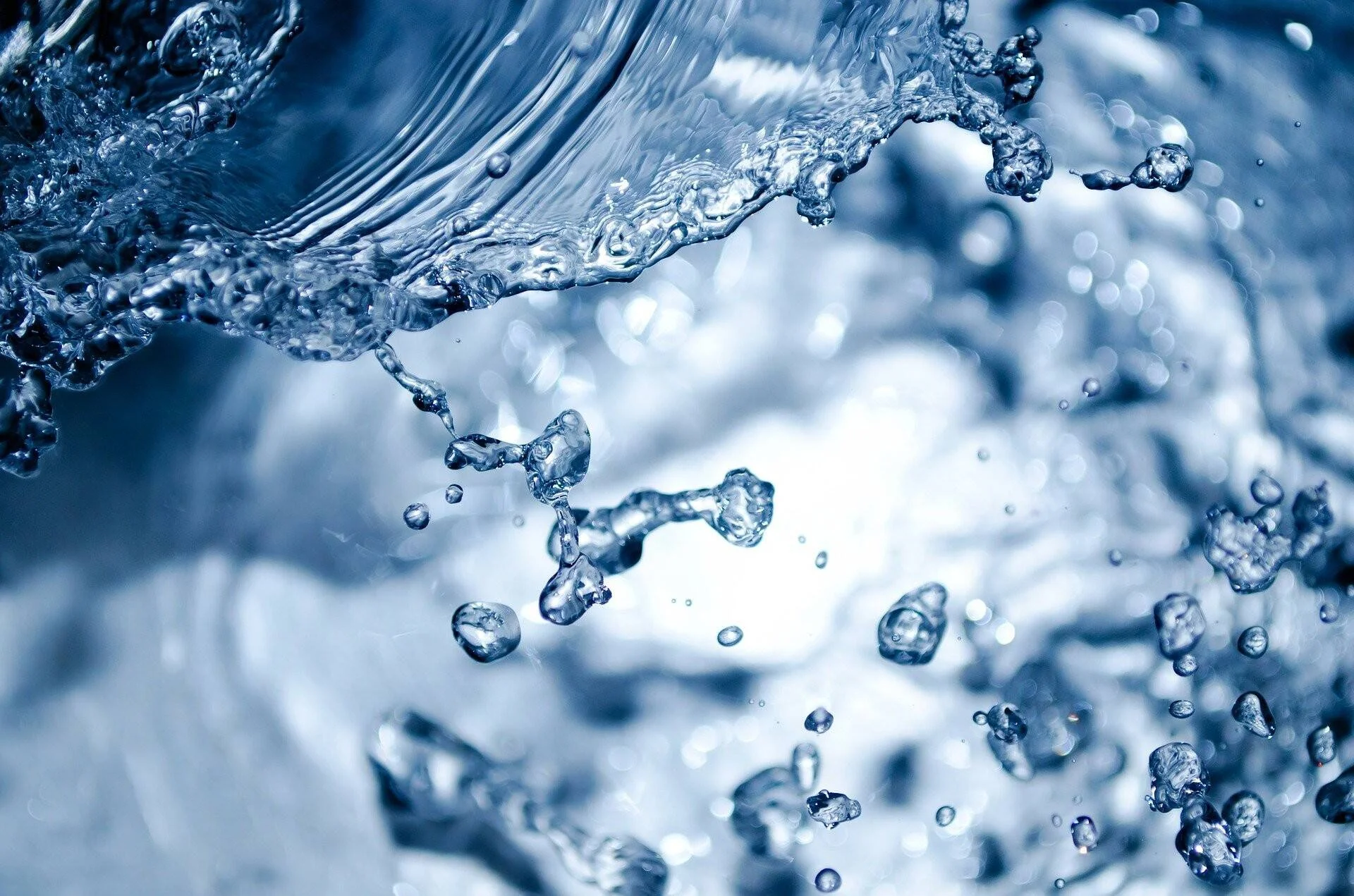Primer plano de agua en movimiento con gotas dispersas suspendidas en el aire sobre fondo azul desenfocado.