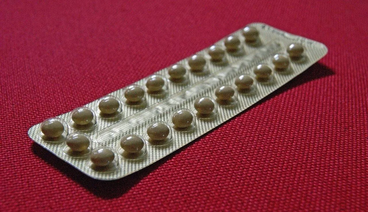 Blíster completo de píldoras anticonceptivas sobre una superficie de tela roja.