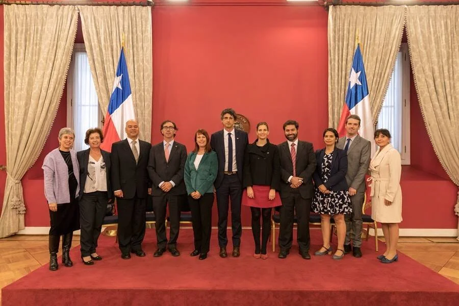 Grupo de once personas posa en un salón oficial con banderas de Chile, en un acto formal de gobierno.