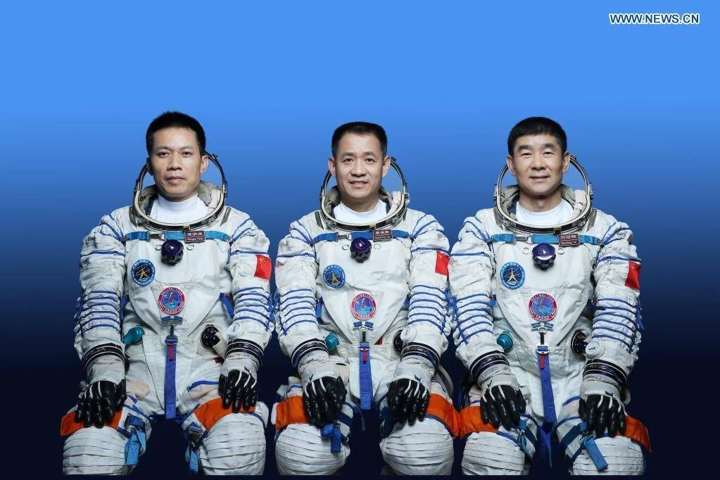 Tres taikonautas chinos con trajes espaciales blancos posan juntos ante un fondo azul para una fotografía oficial de misión.