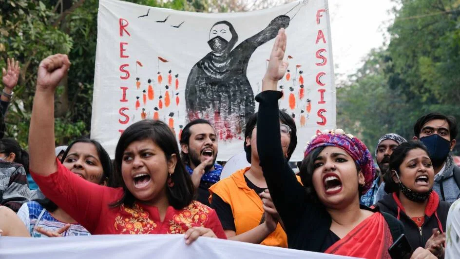 Grupo de jóvenes grita con los puños en alto frente a una pancarta con la consigna 'Resist Fascism' durante una protesta.
