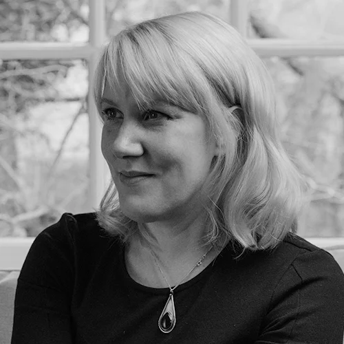 Mujer de cabello rubio corto y collar de gota sonríe levemente en fotografía en blanco y negro.