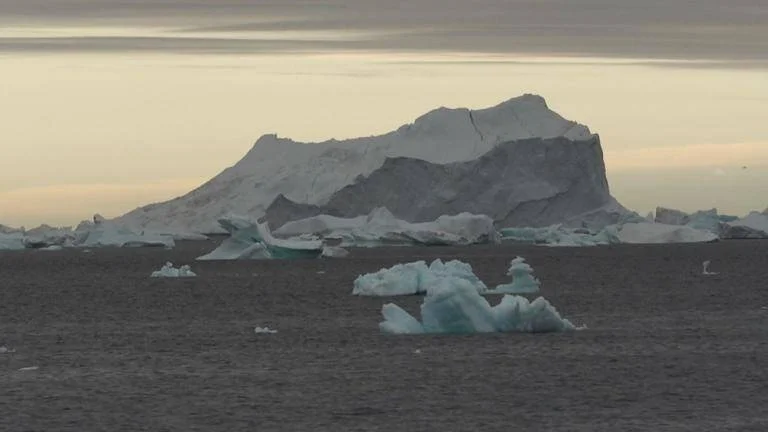 Gran iceberg y fragmentos de hielo flotando en un mar polar bajo un cielo nublado con luz crepuscular.