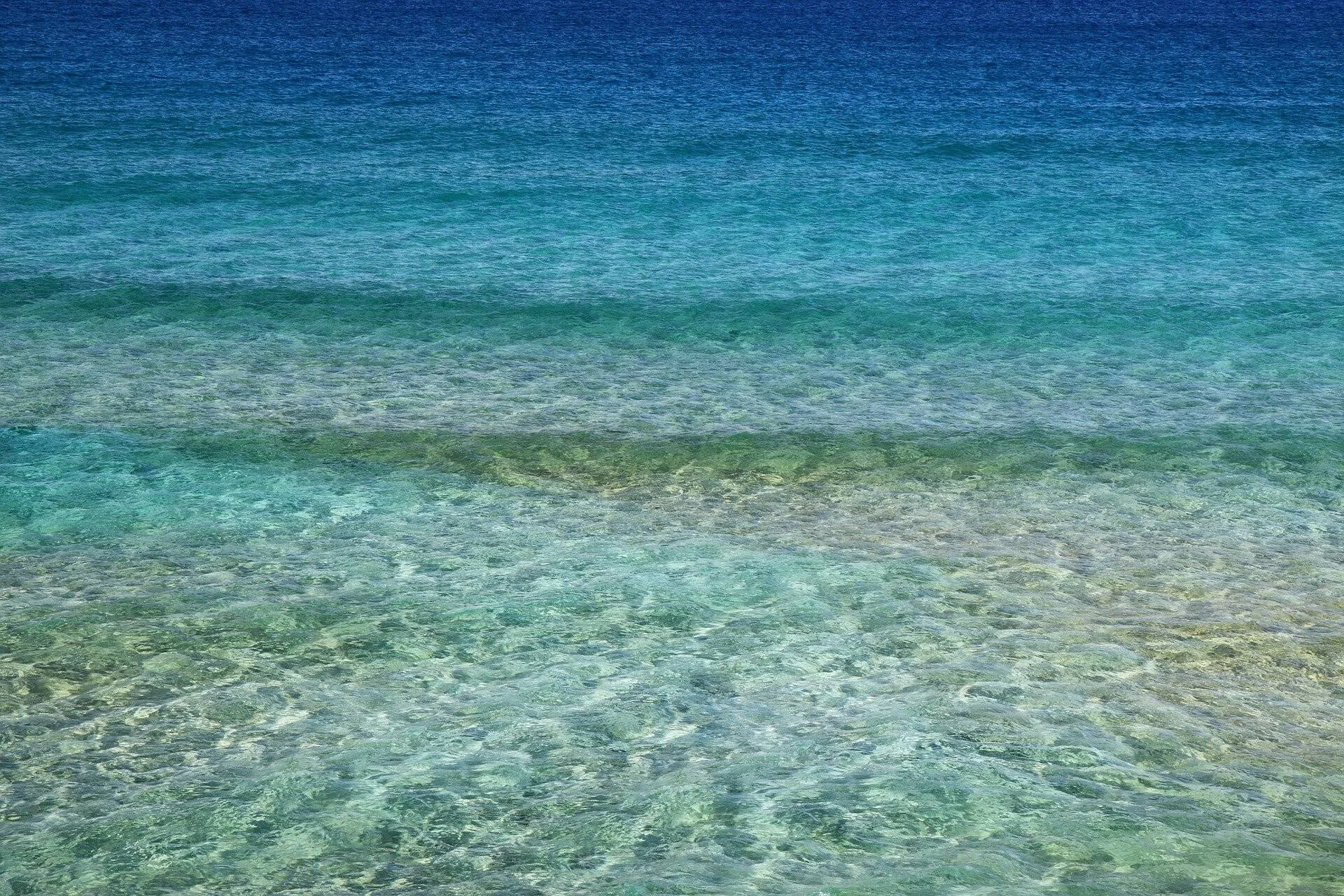 Mar de aguas transparentes con tonos turquesa y verde que revelan el fondo marino en zona costera poco profunda.