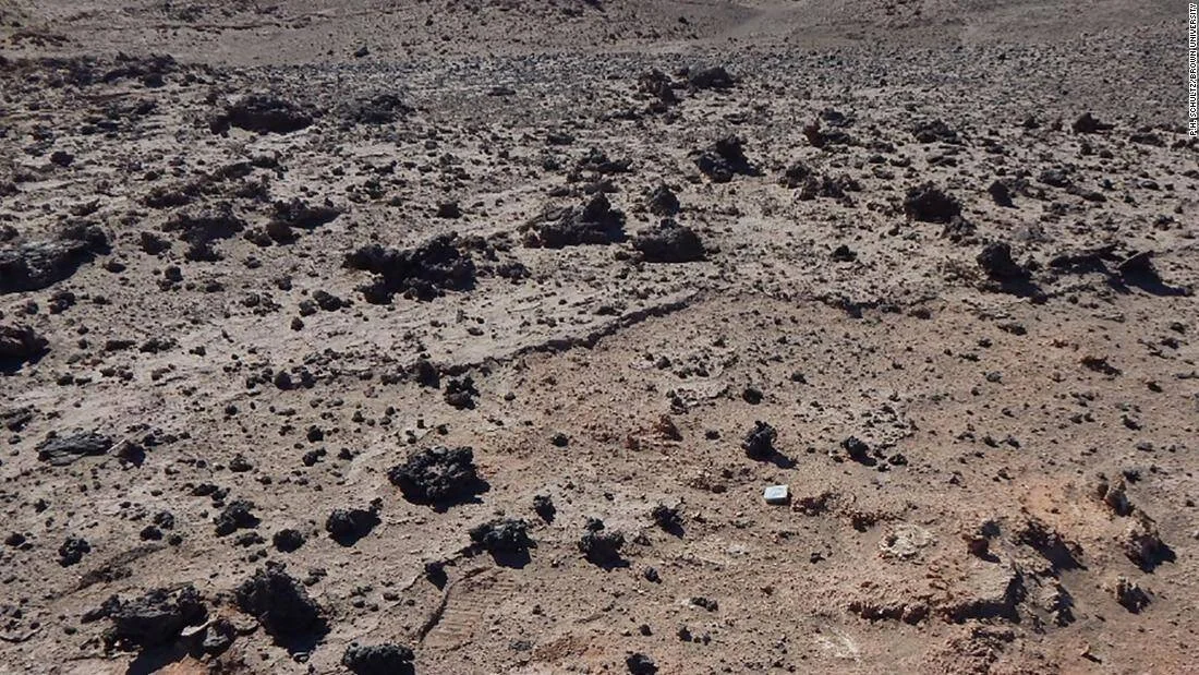 Superficie árida y pedregosa con fragmentos de roca negra dispersos sobre suelo arenoso seco.