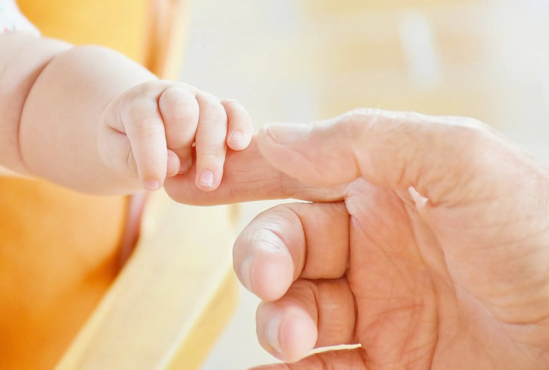 La pequeña mano de un bebé sujeta con fuerza el dedo índice de una mano adulta.