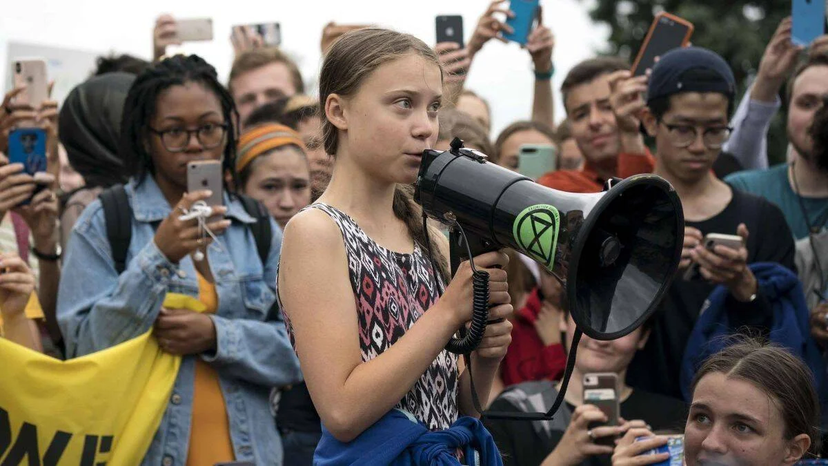 Joven activista habla por un megáfono con símbolo de Extinction Rebellion ante una multitud que graba con sus teléfonos.