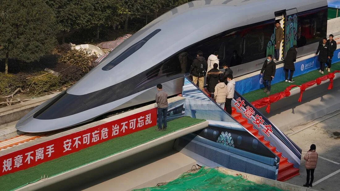 Personas inspeccionan un prototipo de tren de levitación magnética de diseño aerodinámico sobre una plataforma con carteles en chino.