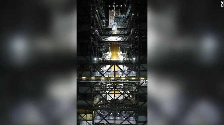 Cohete de la NASA iluminado dentro del edificio de ensamblaje vertical, rodeado de estructuras metálicas de soporte.