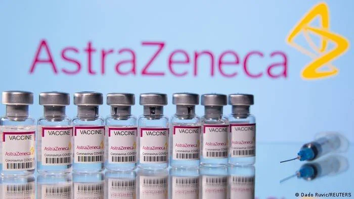Fila de viales de la vacuna AstraZeneca contra el coronavirus junto a jeringas, frente al logo de la compañía.
