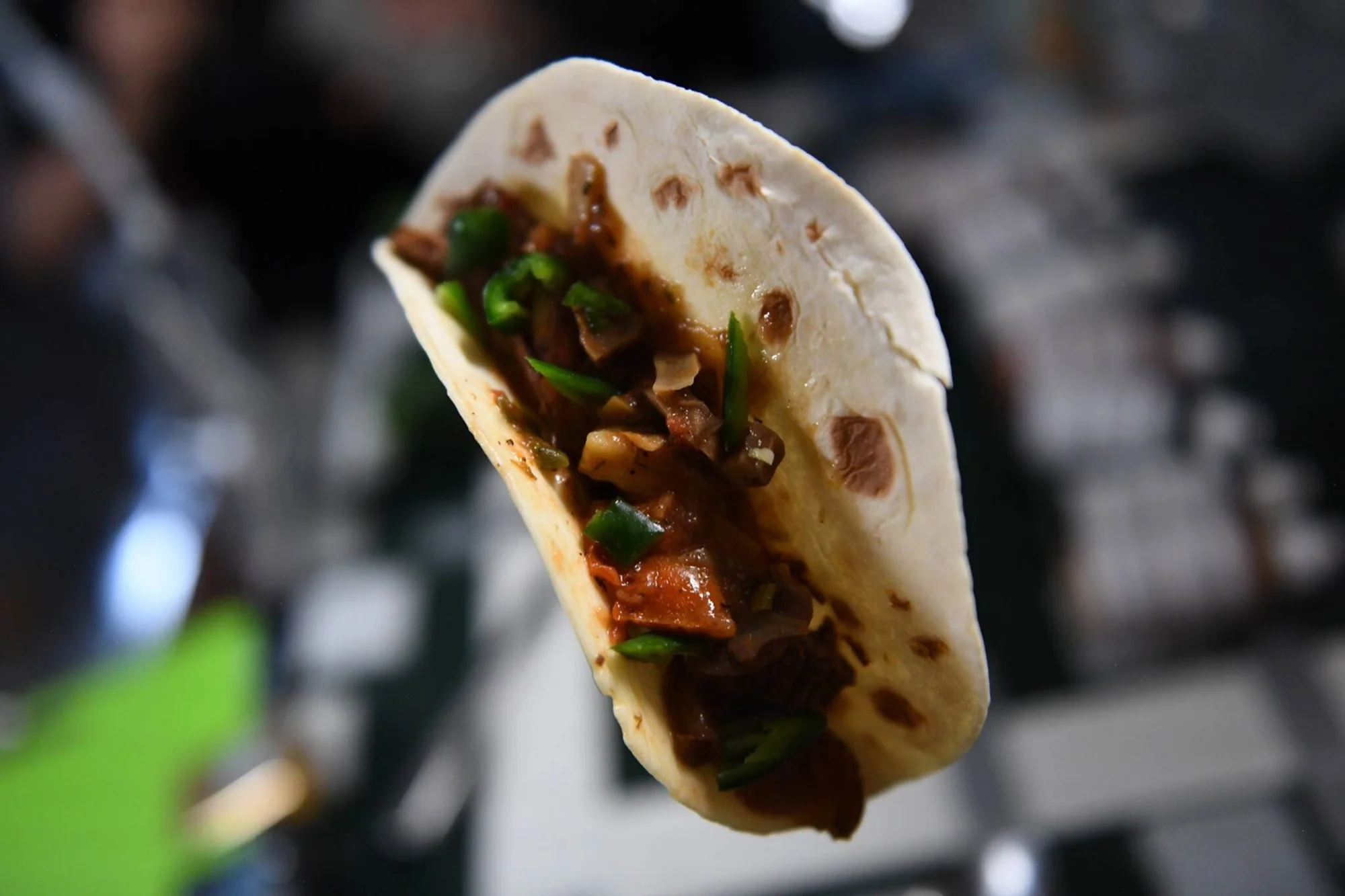 Taco en tortilla de harina relleno de carne guisada con salsa y tiras de chile verde, sostenido en el aire.
