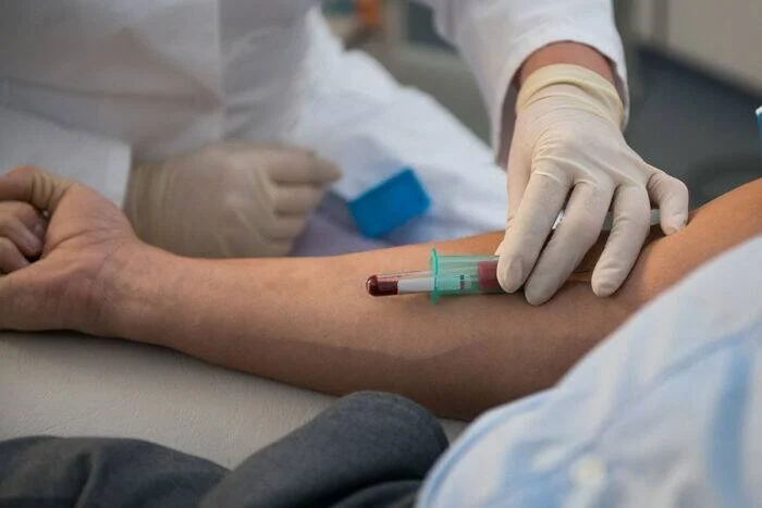 Profesional de salud con guantes extrae una muestra de sangre del brazo de un paciente con una aguja y tubo de análisis.