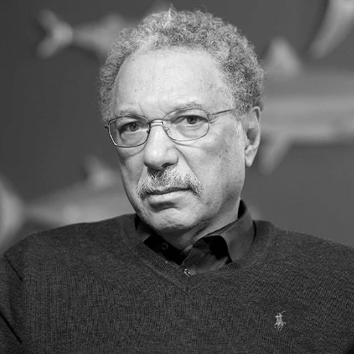 Hombre adulto de cabello canoso y bigote, con gafas y suéter, en fotografía en blanco y negro.