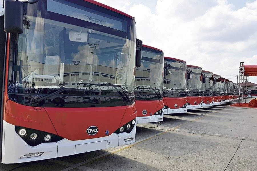 Fila de autobuses urbanos eléctricos de la marca BYD, en rojo y blanco, estacionados en una playa de vehículos.