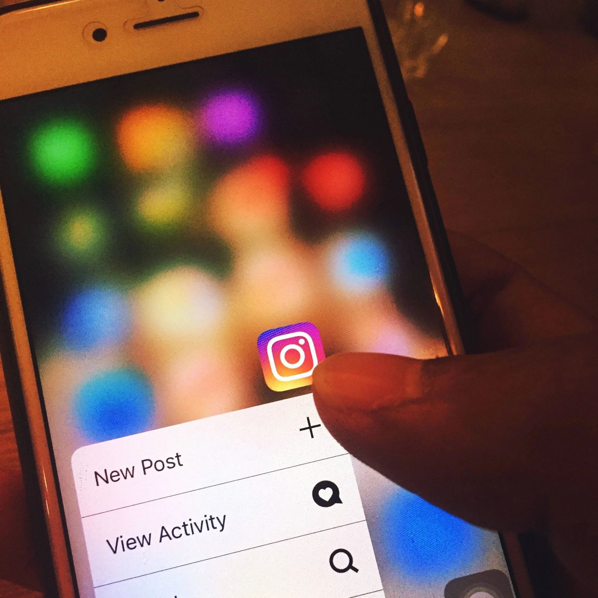 Una mano presiona el ícono de Instagram en un teléfono móvil, mostrando el menú rápido con opciones New Post y View Activity.