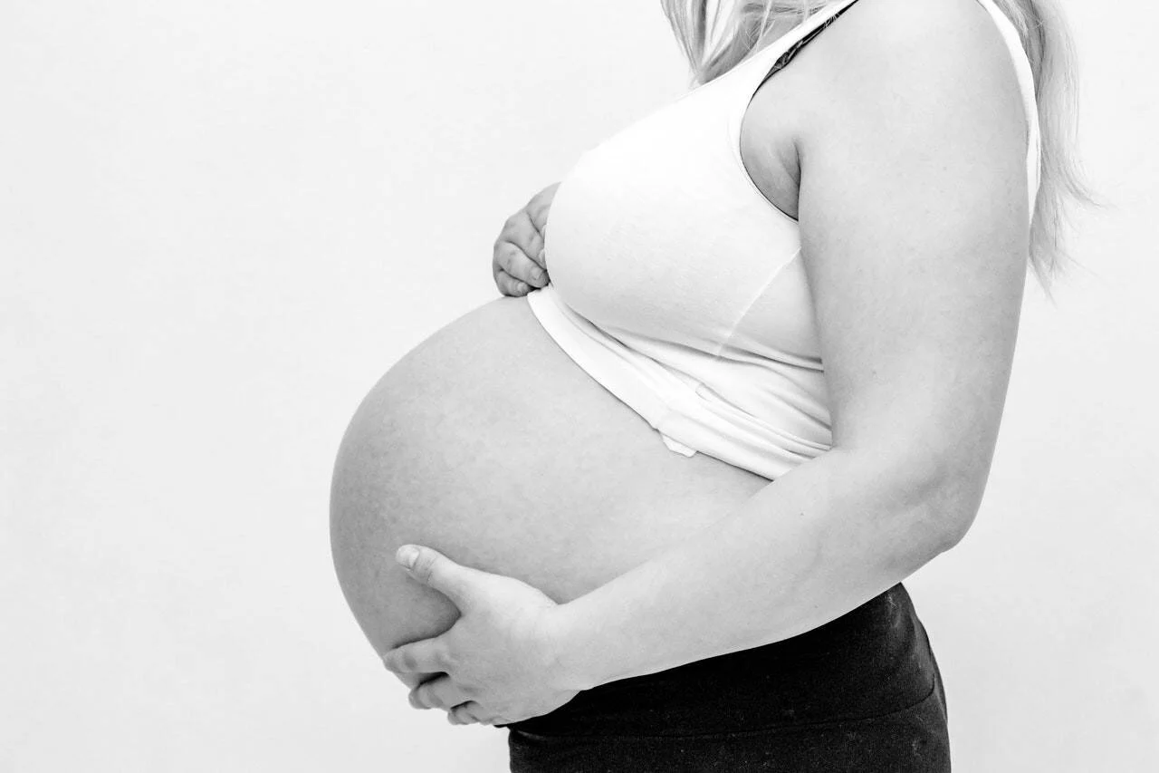 Mujer embarazada de perfil sostiene su vientre con ambas manos, fotografía en blanco y negro.