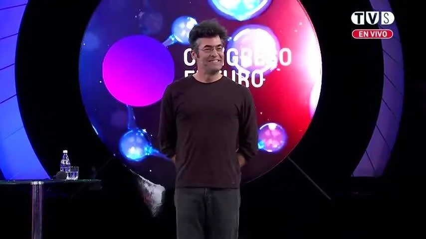 Hombre sonriente de pie en el escenario del Congreso Futuro, transmitido en vivo por TVS.