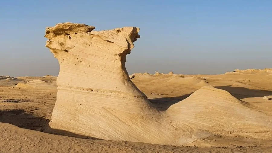 Gran roca de arenisca con forma de hongo tallada por la erosión eólica en un paisaje desértico bajo cielo despejado.