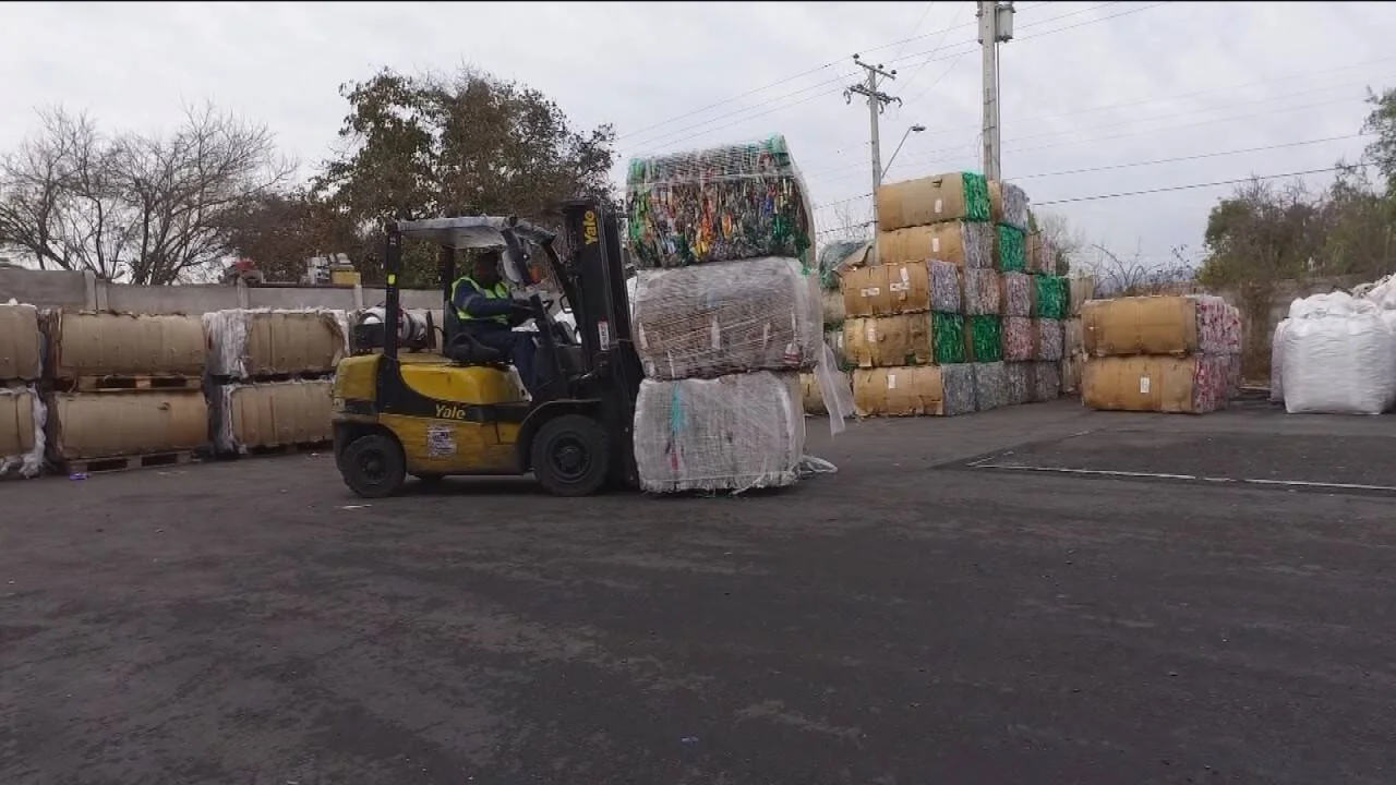 Un autoelevador Yale mueve fardos compactados de plástico y papel en un centro de reciclaje rodeado de grandes pilas de materiales.