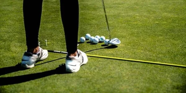 Golfista de pie sobre el green con varias pelotas y un palo de golf alineados para practicar putting.