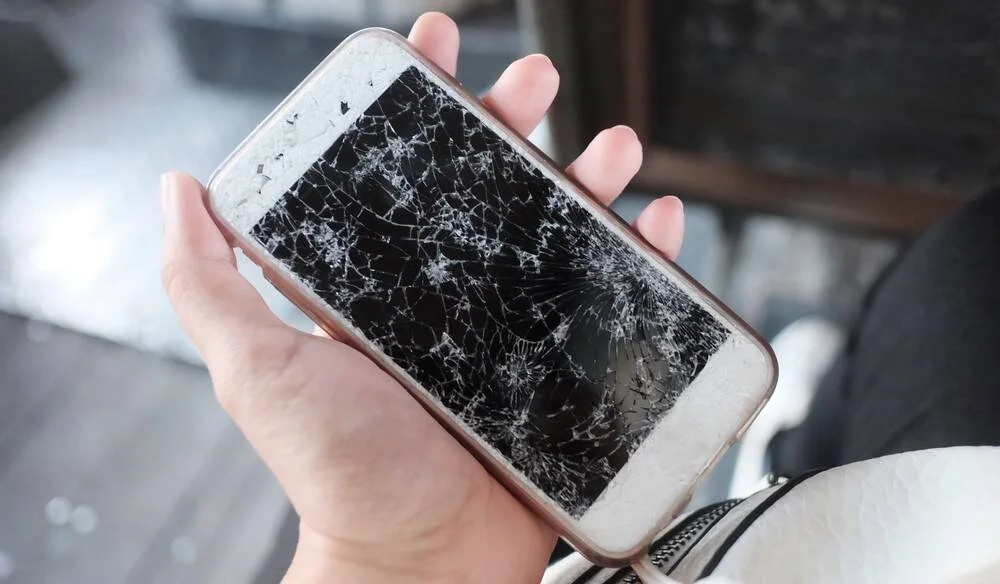 Una mano sostiene un teléfono inteligente con la pantalla totalmente agrietada y destrozada.