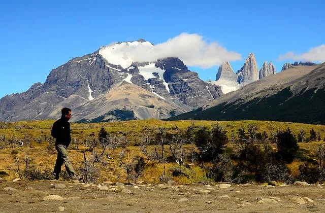 Persona caminando en la estepa patagónica con las torres y macizos nevados de Torres del Paine al fondo.