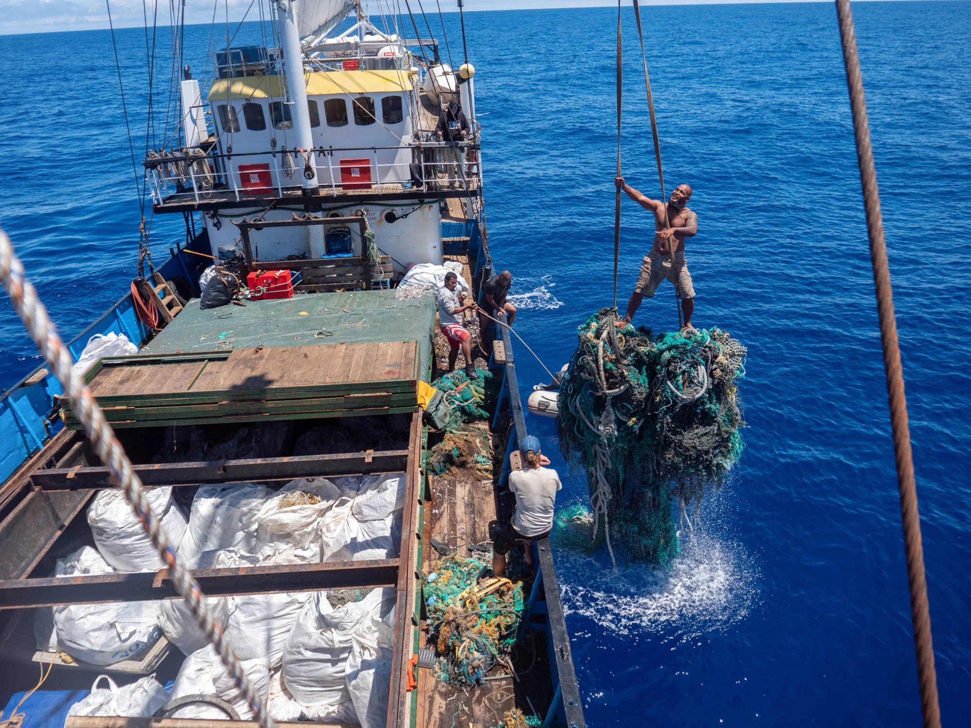 Trabajadores a bordo de un barco izan una gran masa de redes de pesca abandonadas recuperadas del océano Pacífico.
