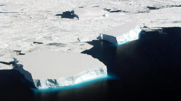 Vista aérea de grandes icebergs tabulares con paredes verticales azules rodeados de hielo marino fragmentado en aguas oscuras.